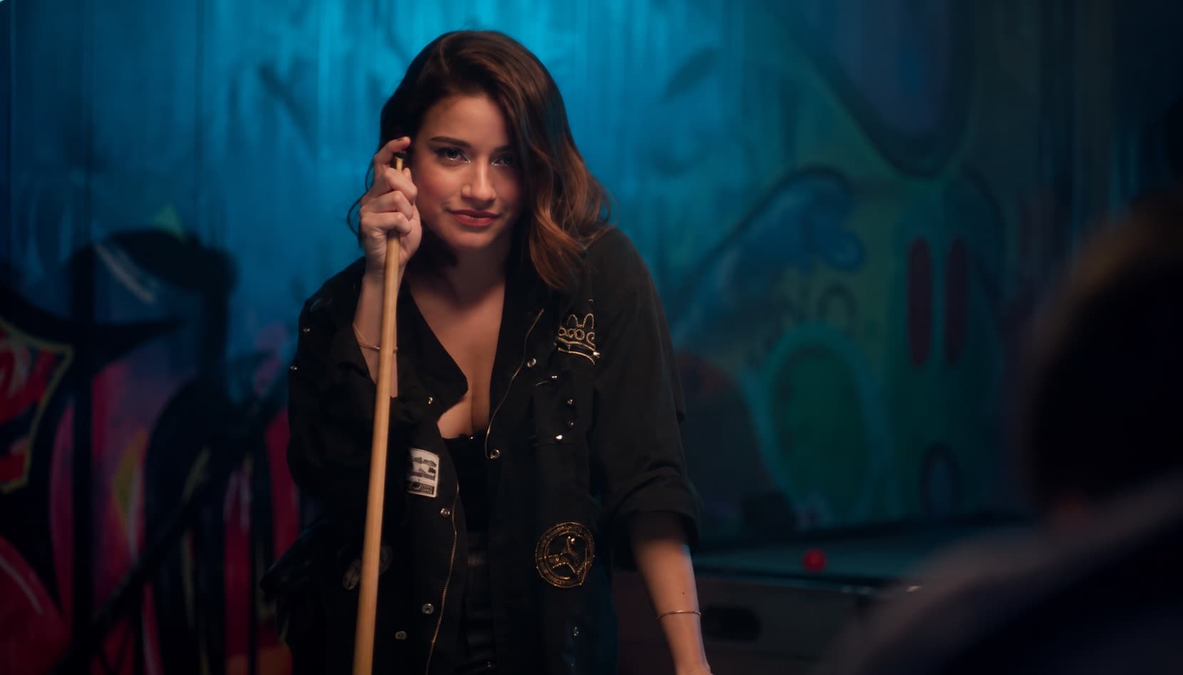 Scène de clip : actrice avec une queue de billard devant une fresque de graffiti