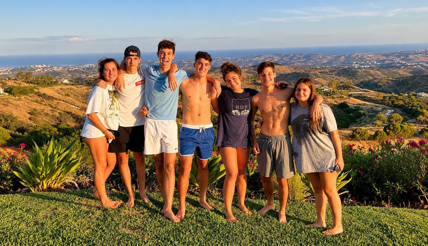 Groupe d'amis dans le jardin au coucher du soleil, avec la mer et la côte en fond