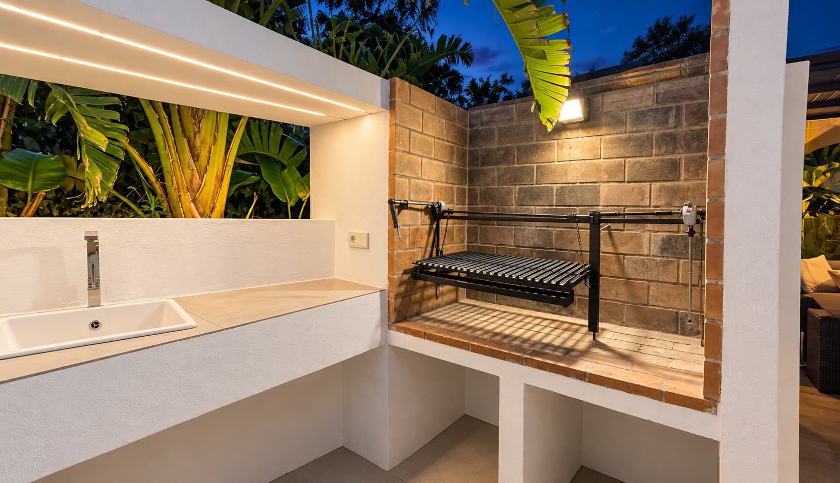 Barbecue en dur avec grill, évier et mur de briques à la tombée de la nuit